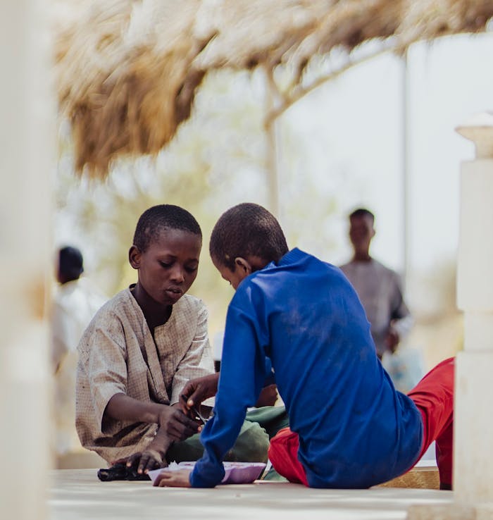 Two children playing with a game outdoors under a thatched roof.